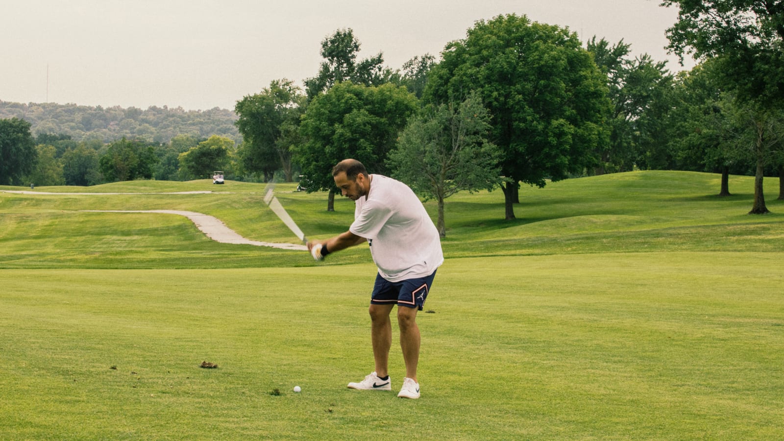 Golfer's full follow-through against a wide stretch of fairway and tree line