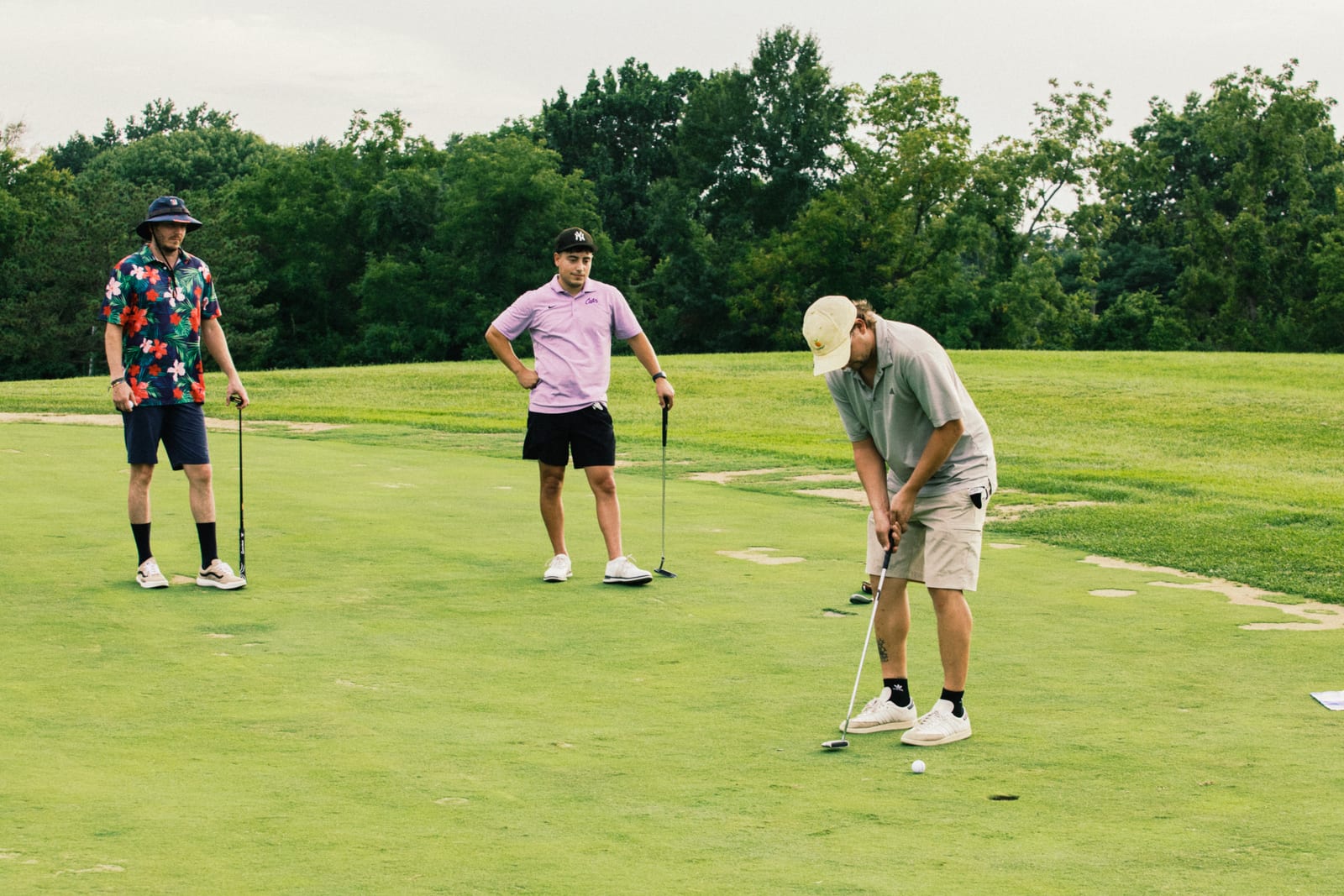 Three golfers gathered on the green, one in a camo jacket watching the putt