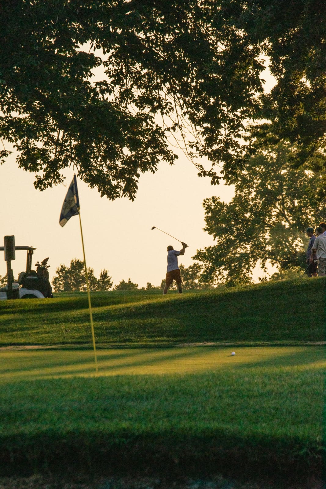 Flagstick silhouetted against a golden dusk sky at the end of the round