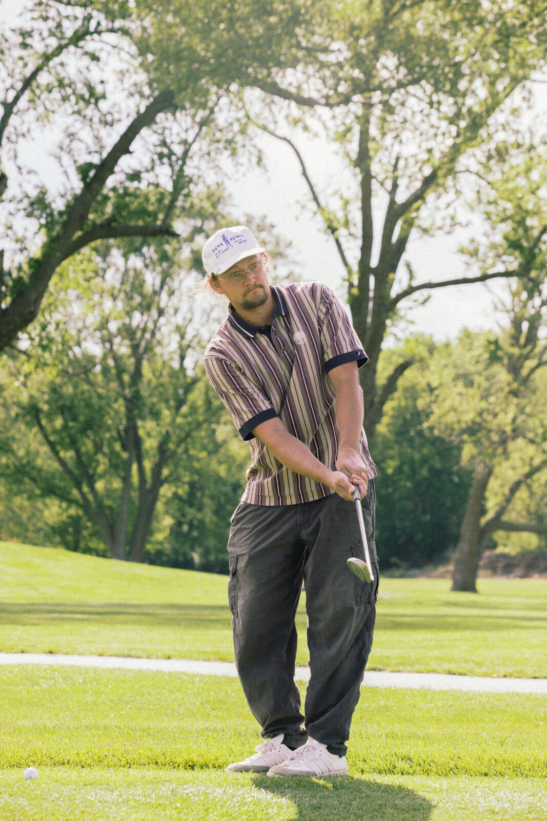 Golfer in striped polo and cap mid-chip on the fairway