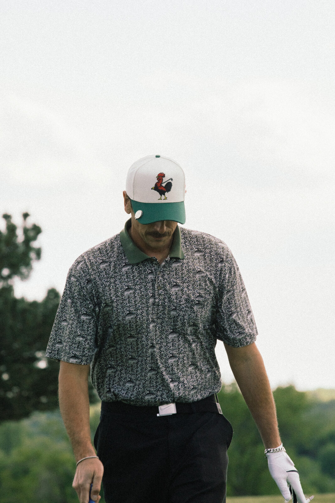 Golfer in printed shirt and rooster cap walking the course