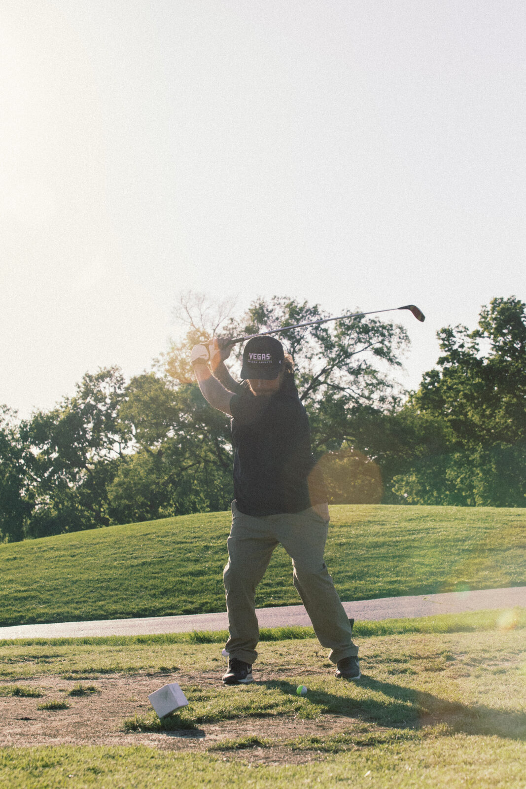 Golfer mid-swing silhouetted against sun flare on the tee