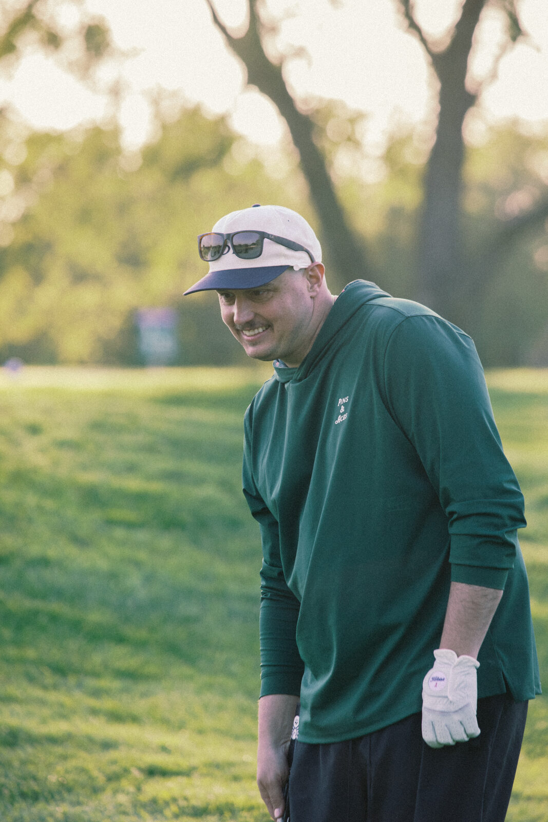 League member smiling on the green at golden hour, green long sleeve