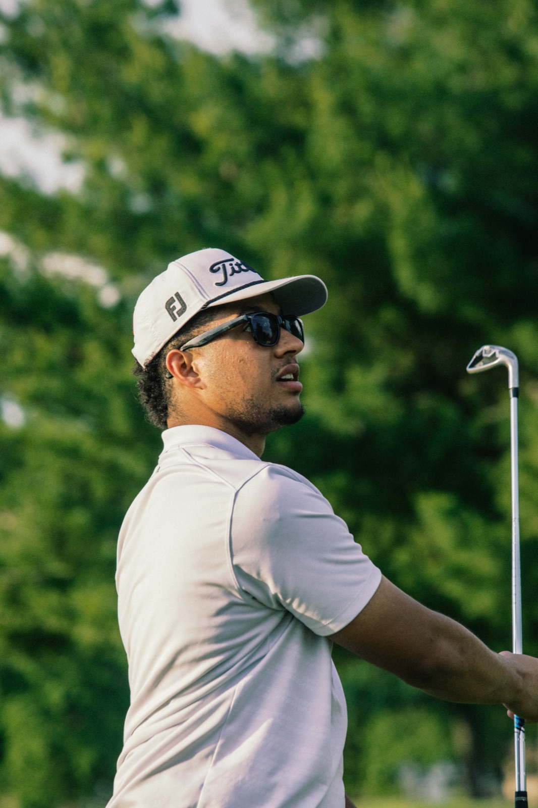 Player in a white polo and cap glancing back between shots