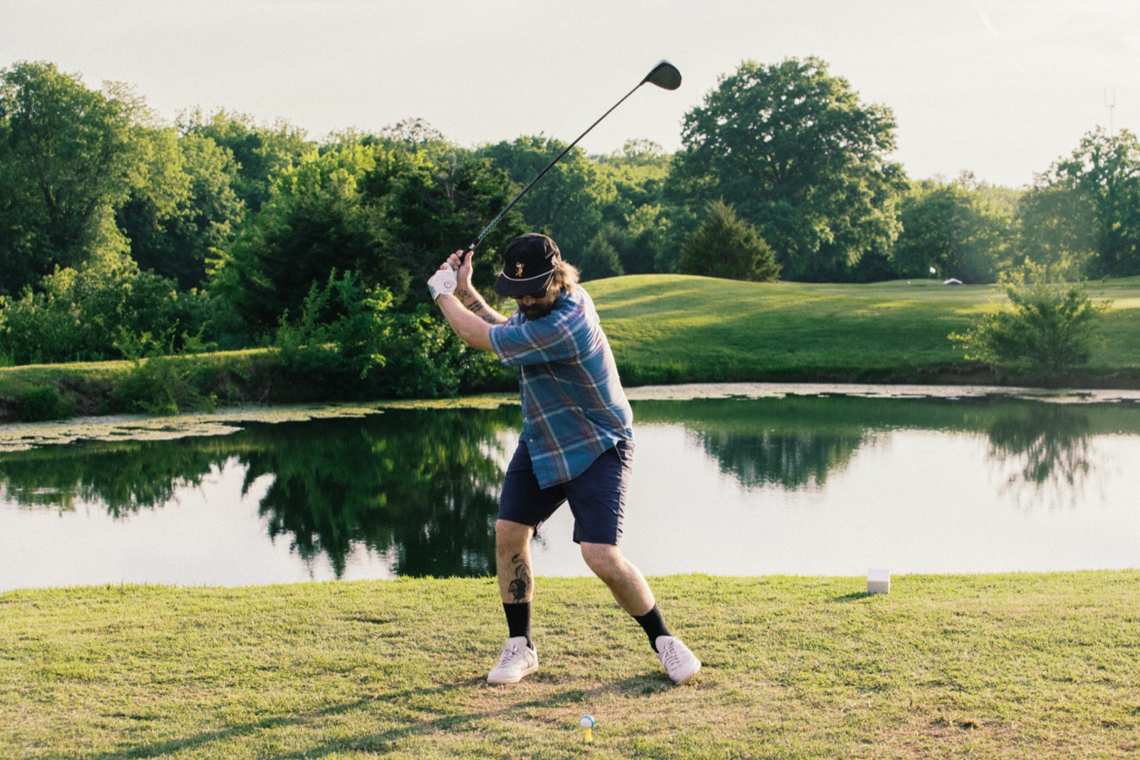 Golfer mid-swing reflected over the pond at golden hour