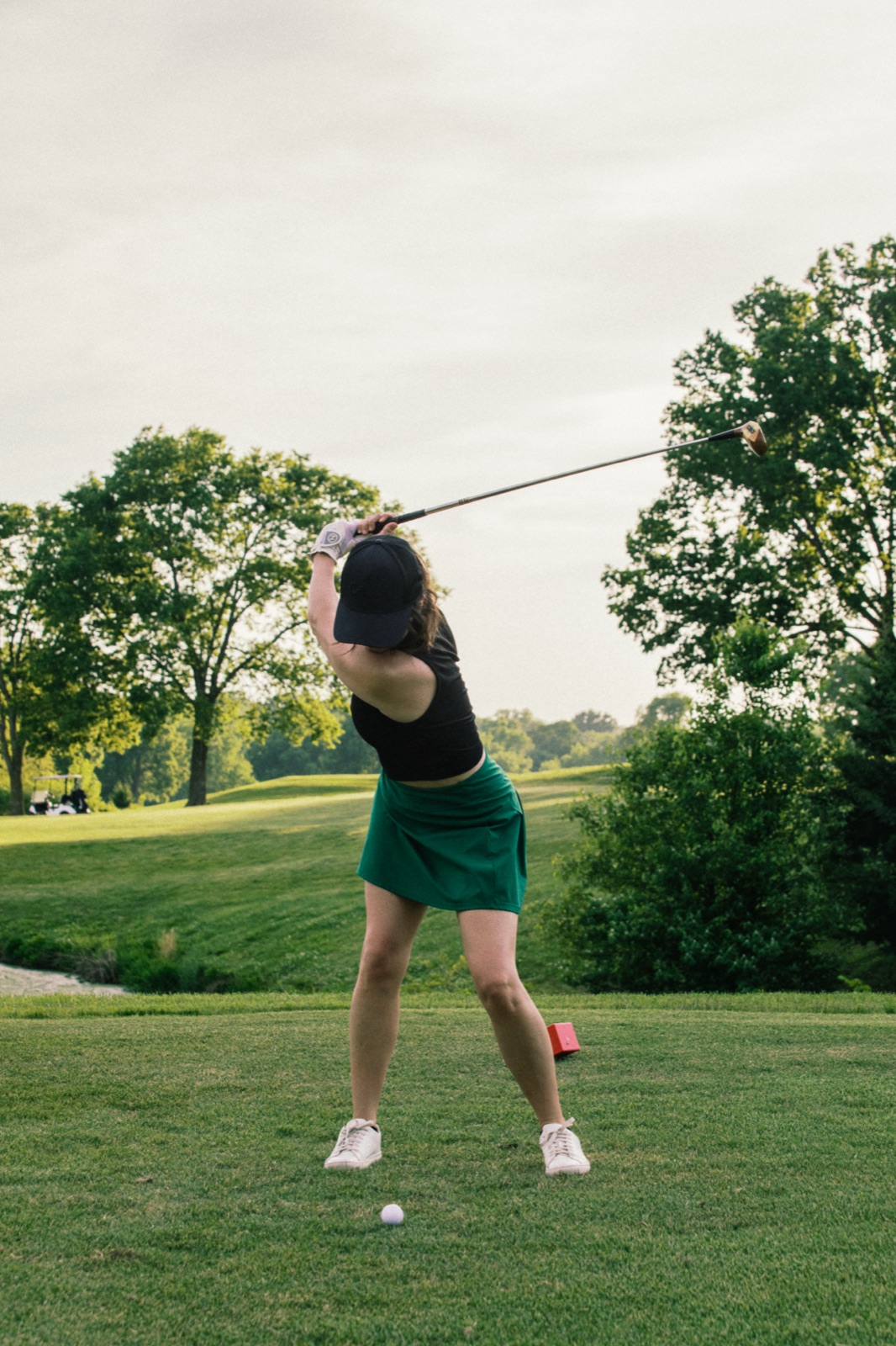 Golfer mid-swing in a green skirt at golden hour