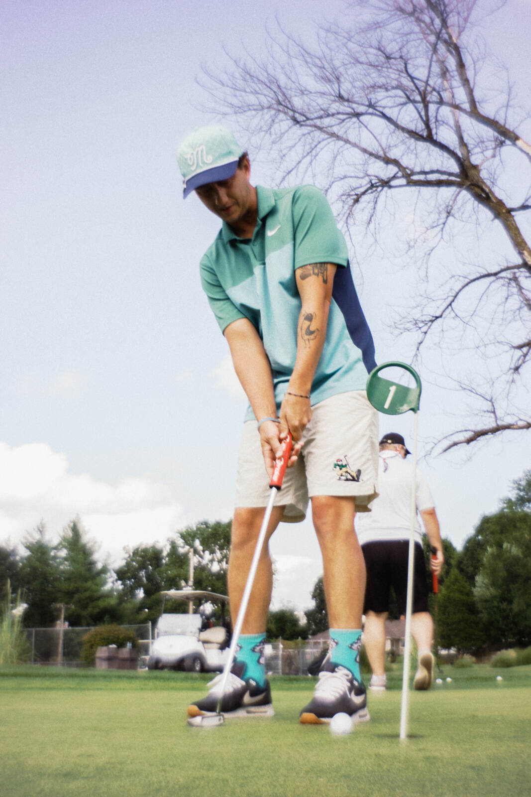League member in a mint M cap and teal polo standing over a putt beside the flag