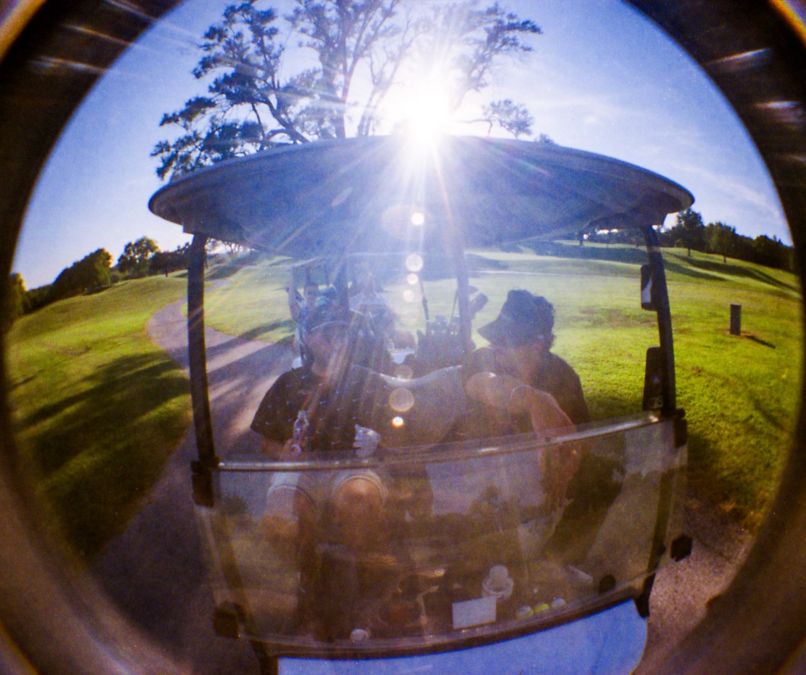 Two league members backlit under the cart canopy as the sun flares through the trees