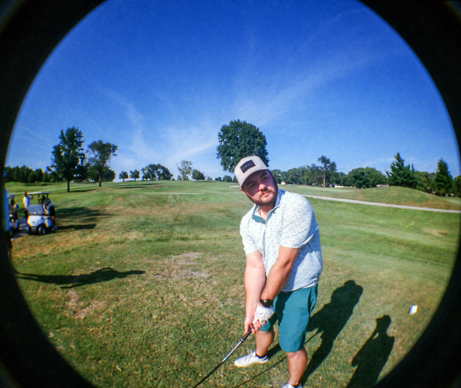 Golfer in a patterned polo and cap watching his tee shot climb