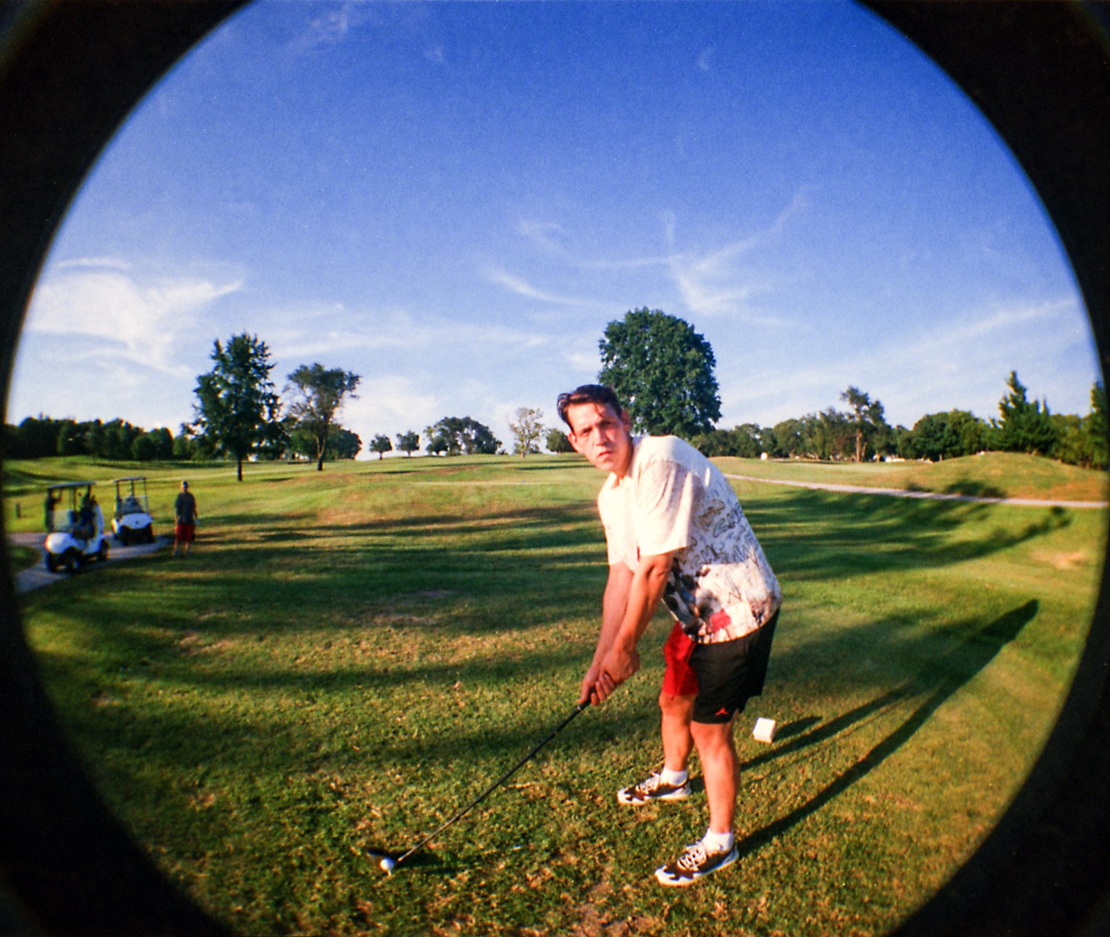 Player in a graphic tee squaring up over the ball at the tee box