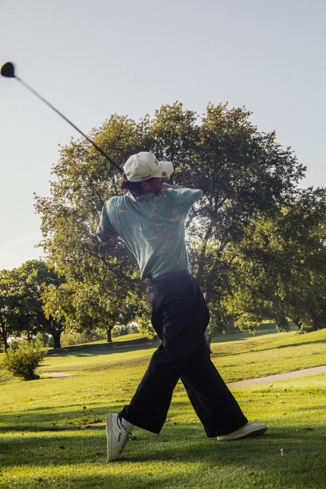 Golfer in a teal polo and black pants at the top of his drive
