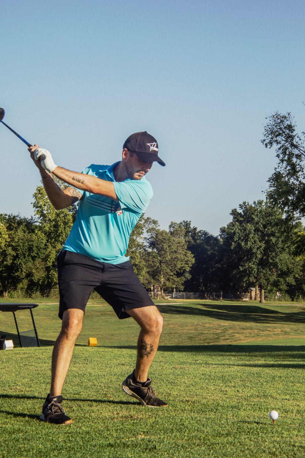 Golfer in a teal tee and cap mid backswing with the driver