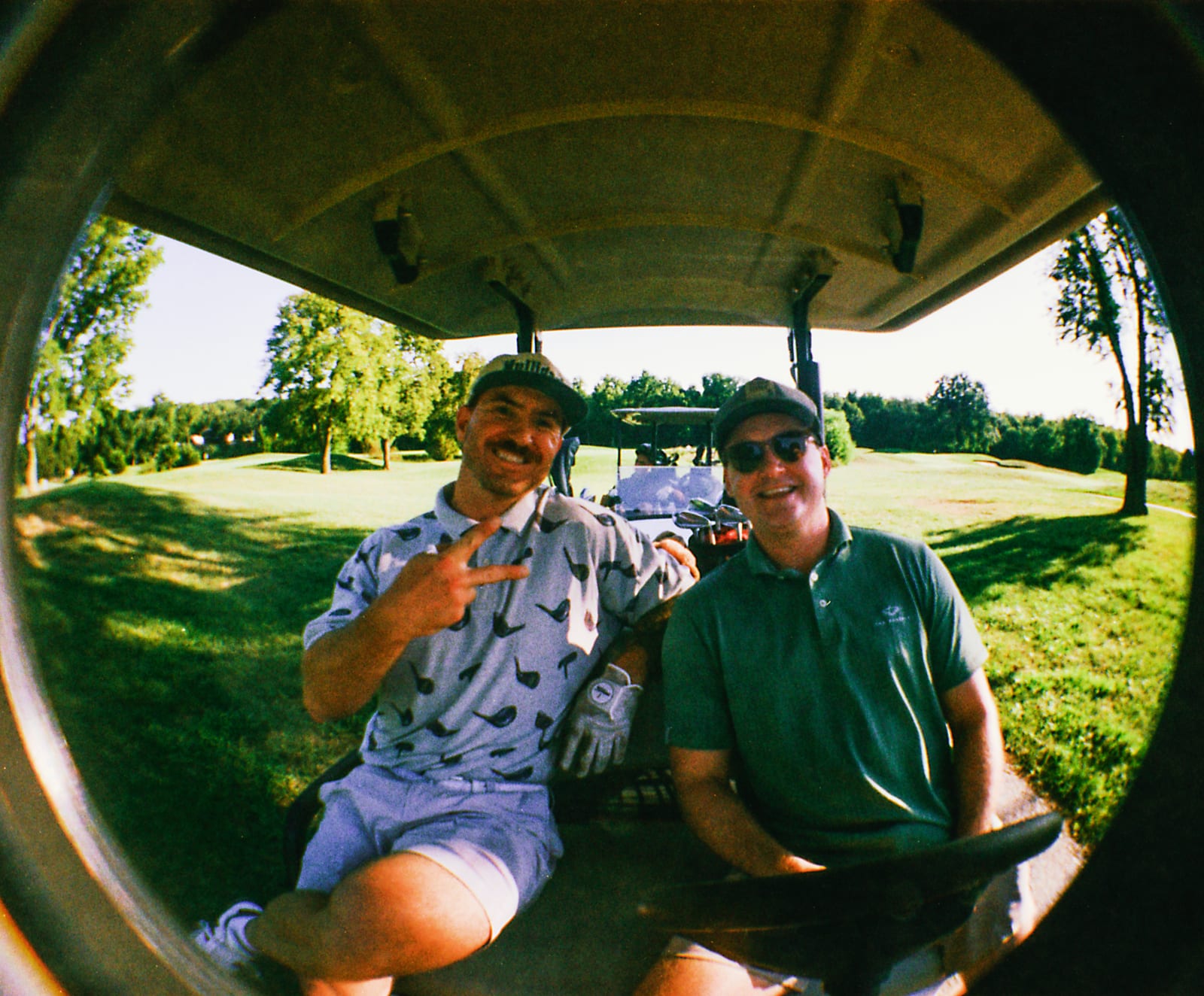 Two players in a cart, one flashing a peace sign, shot fisheye